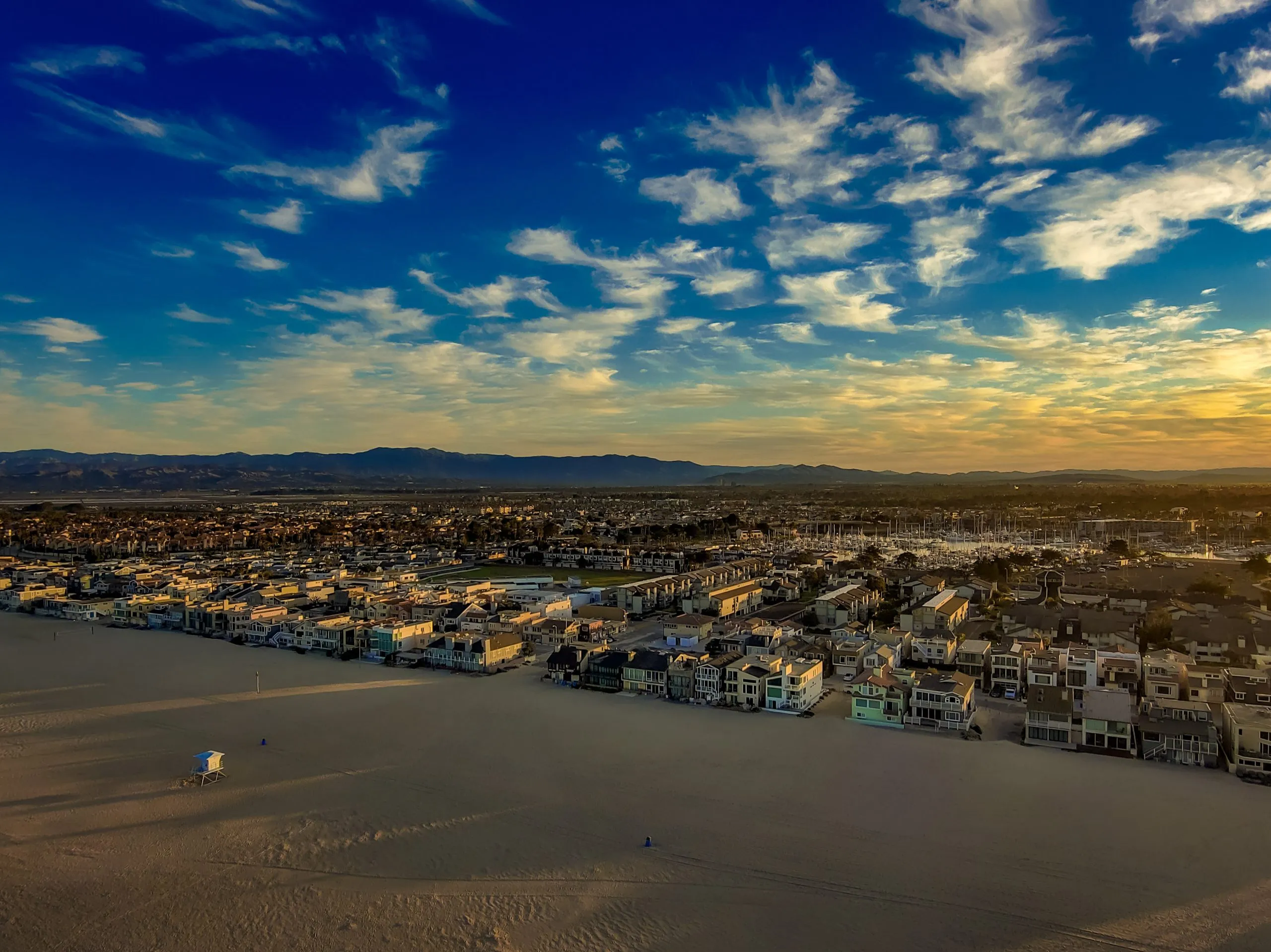 Aerial view of a coastal cityscape with sandy beaches and vibrant sunset skies.