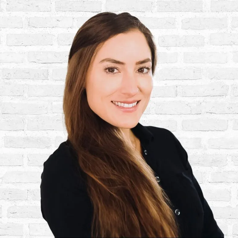 Smiling woman with long hair in front of a white brick wall.