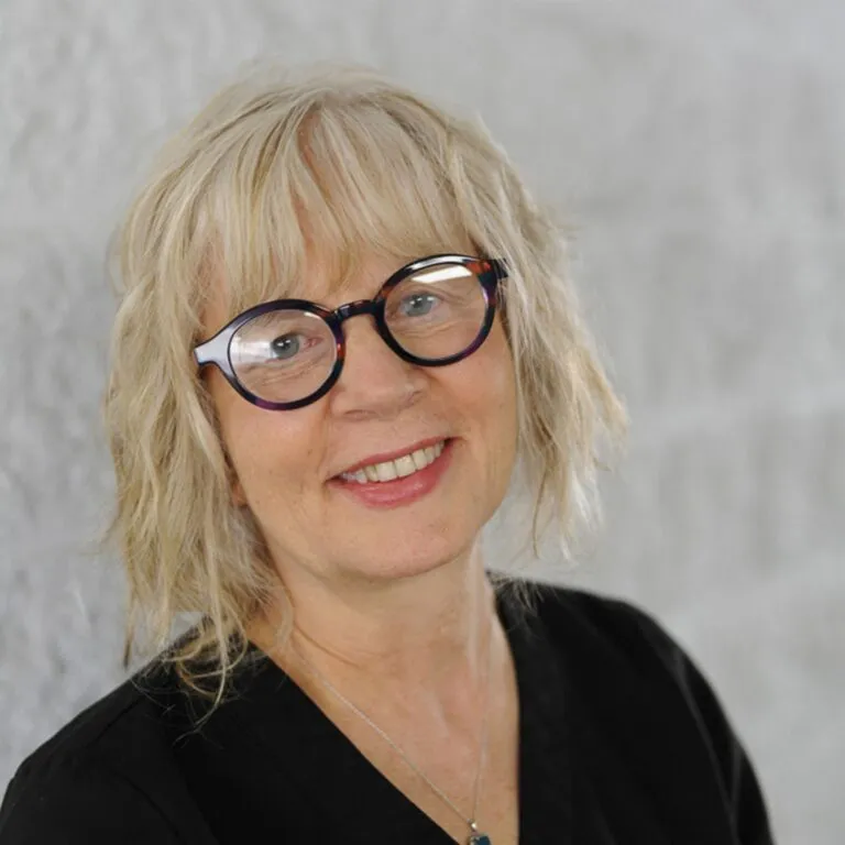 Smiling woman with glasses and blonde hair against a light background.