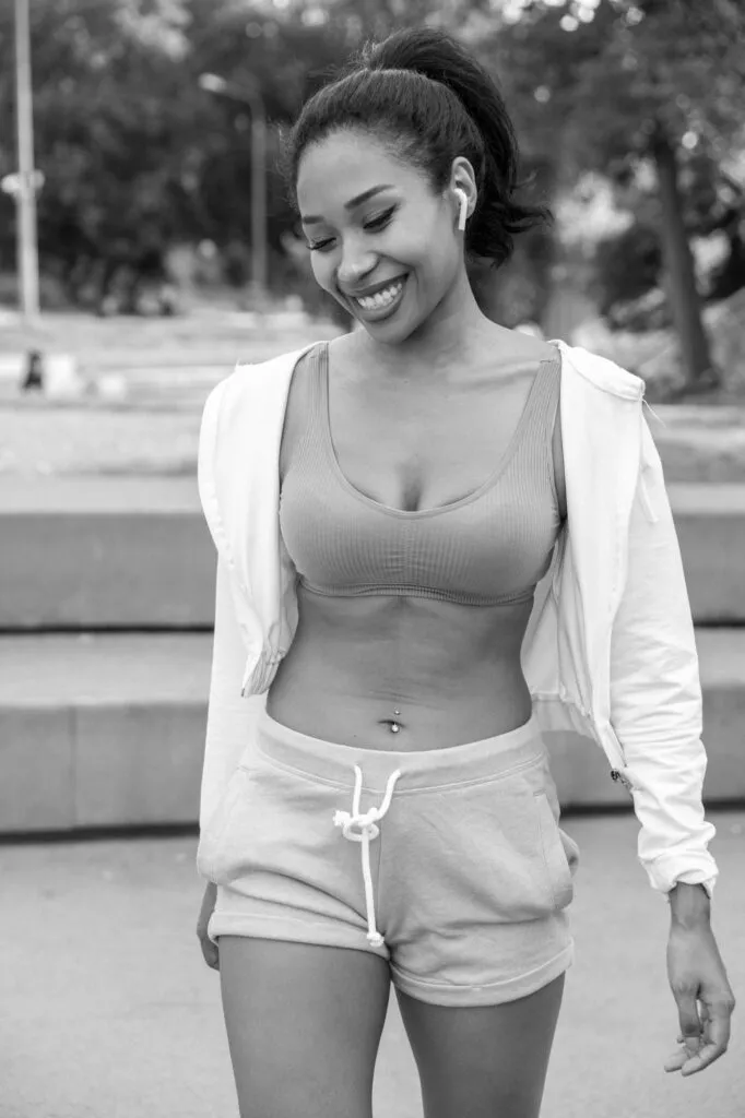 Smiling woman in athletic wear walking outdoors, showcasing toned body and confident appearance.
