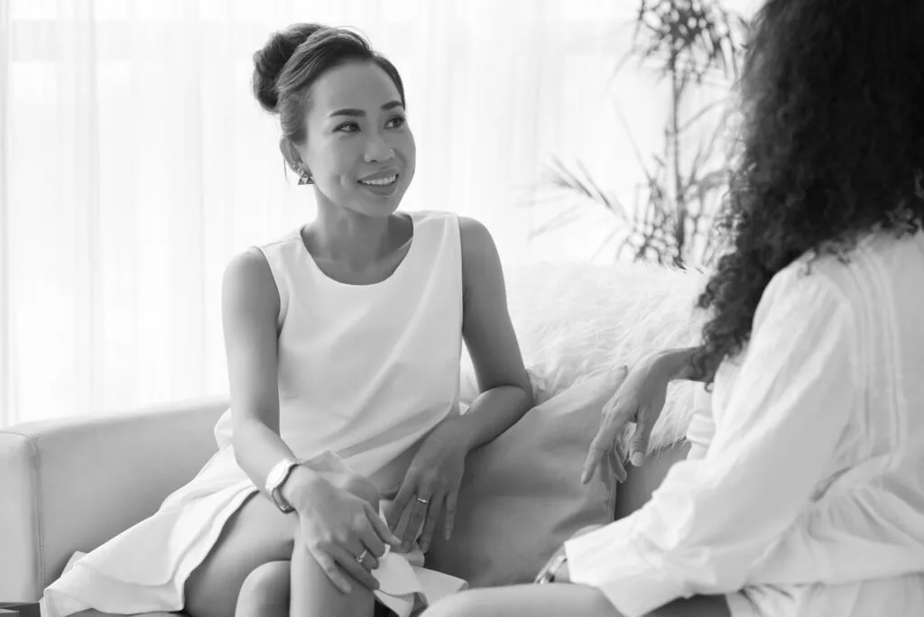 Two women sitting and talking in a modern, comfortable setting at a plastic surgery consultation.