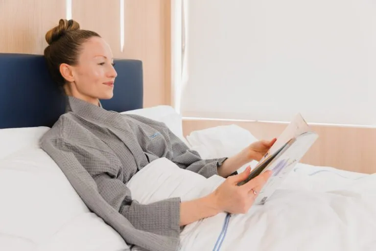Woman in recovery at a plastic surgery center, relaxing and reading in bed.