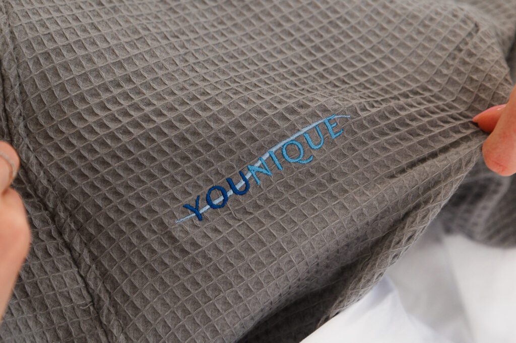 Gray fabric with "YOUNIQUE" embroidered, held by a hand.
