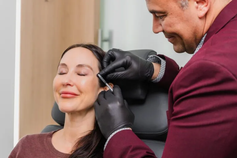 Doctor performing cosmetic injection on smiling woman at plastic surgery center.