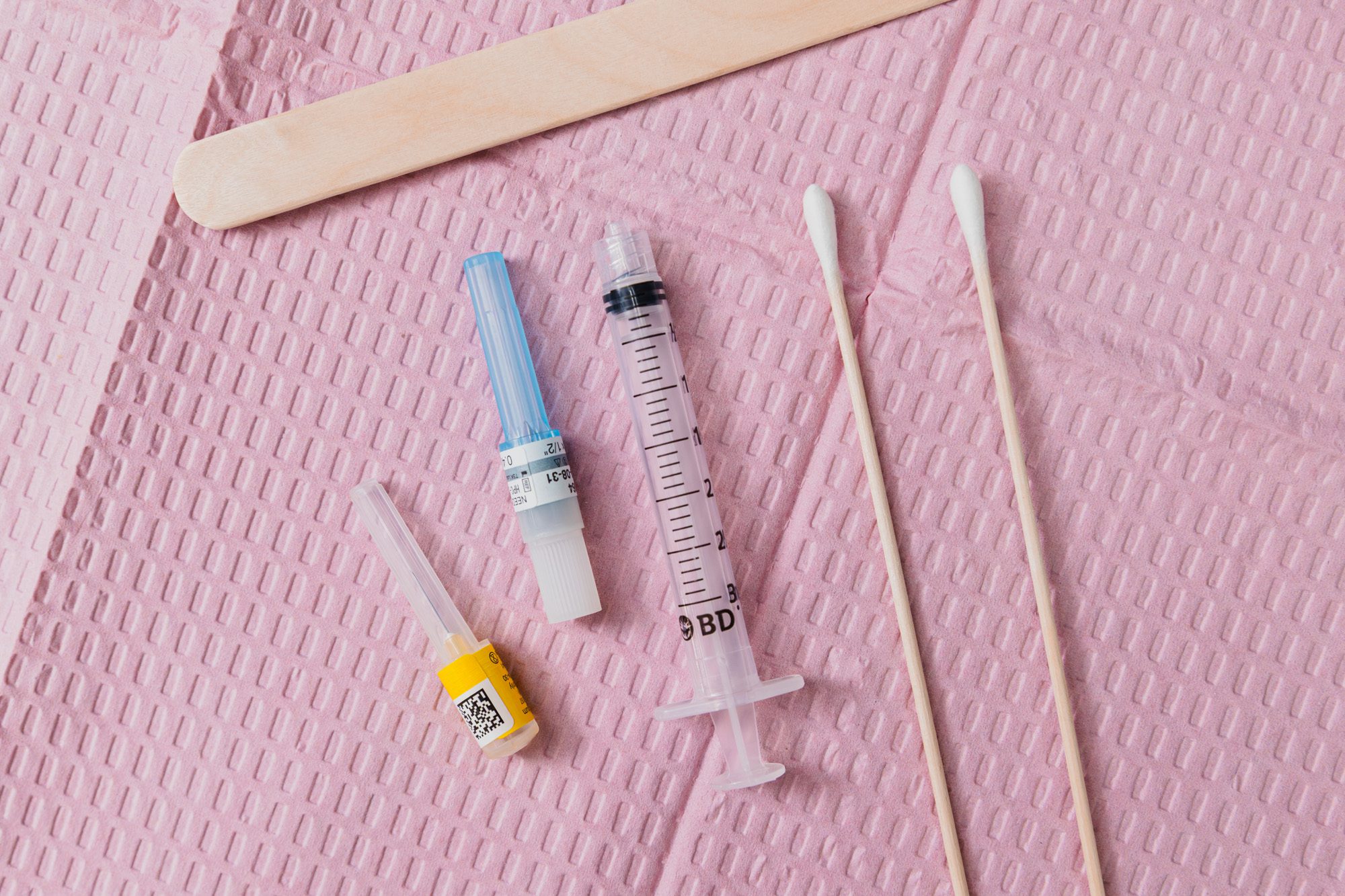 Medical tools and syringe on a pink textured background.