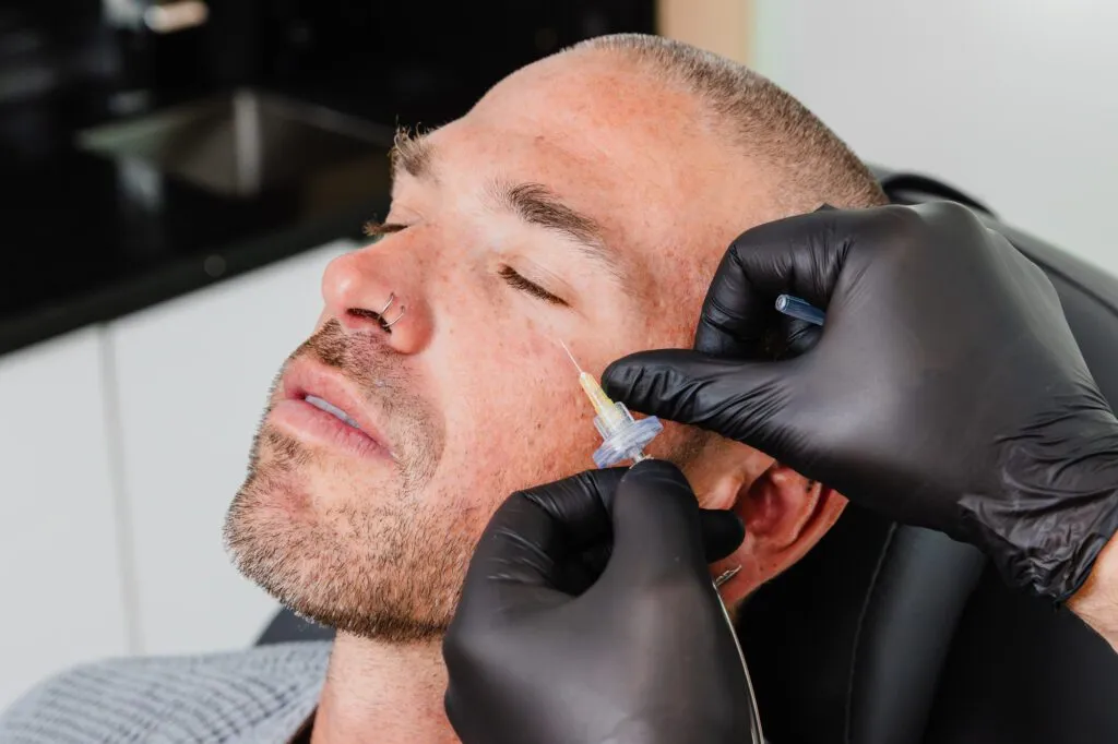 Man receiving cosmetic injection in face at plastic surgery center.