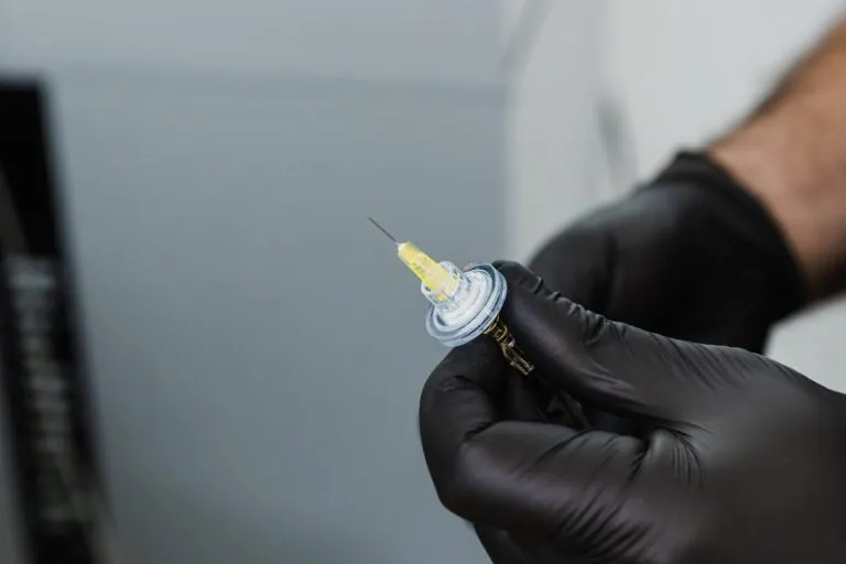 Close-up of a black-gloved hand holding a medical syringe, representing precision and care at a plastic surgery center.