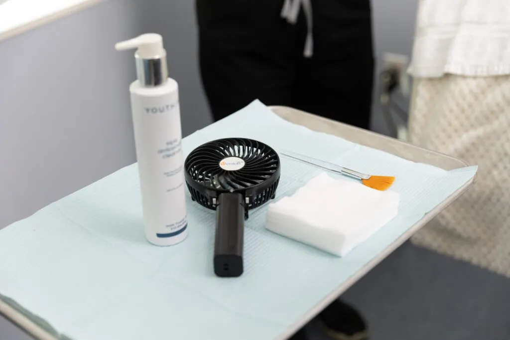 Surgical tray with skincare cleanser, handheld fan, brush, and gauze pads at a plastic surgery center.