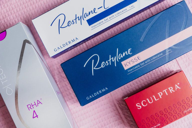 Restylane and Sculptra cosmetic injectable packaging on pink textured background.