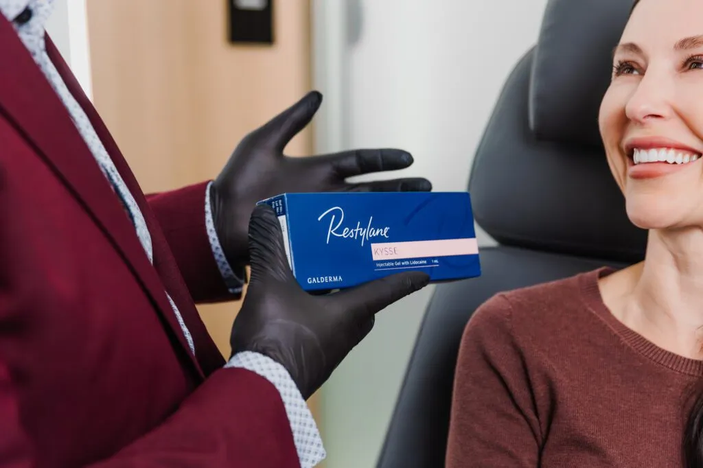 Plastic surgeon holding Restylane Kysse dermal filler package near smiling patient.