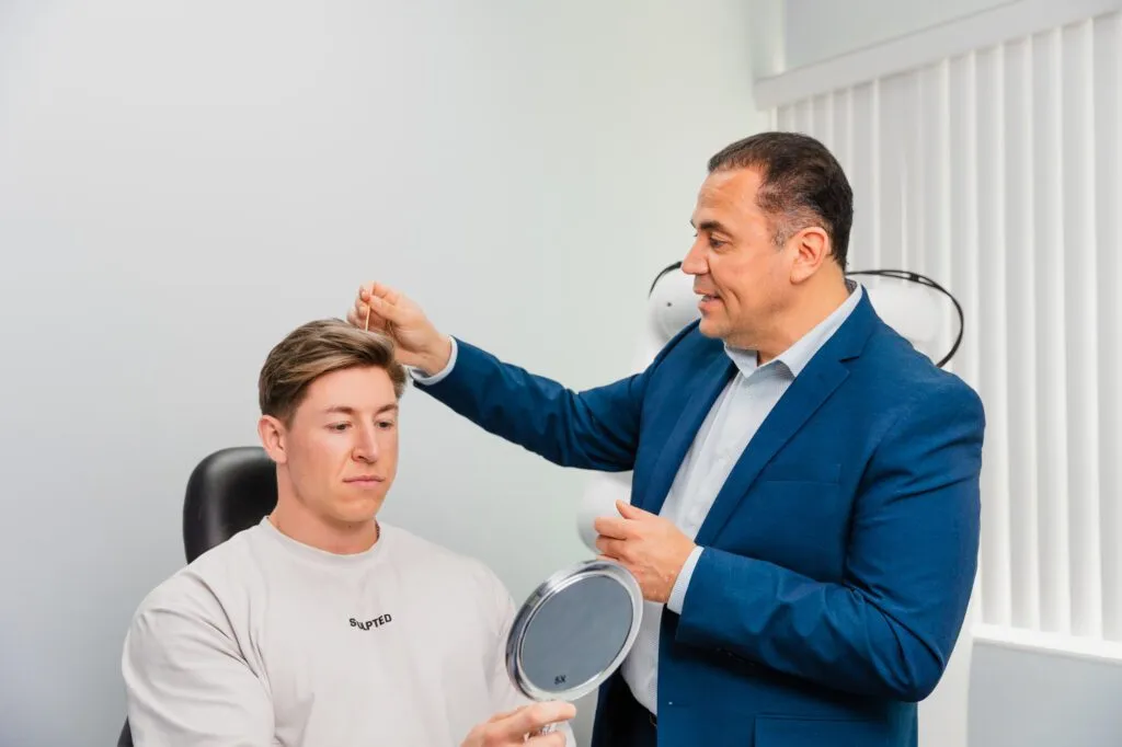 Plastic surgeon consulting male patient with mirror.