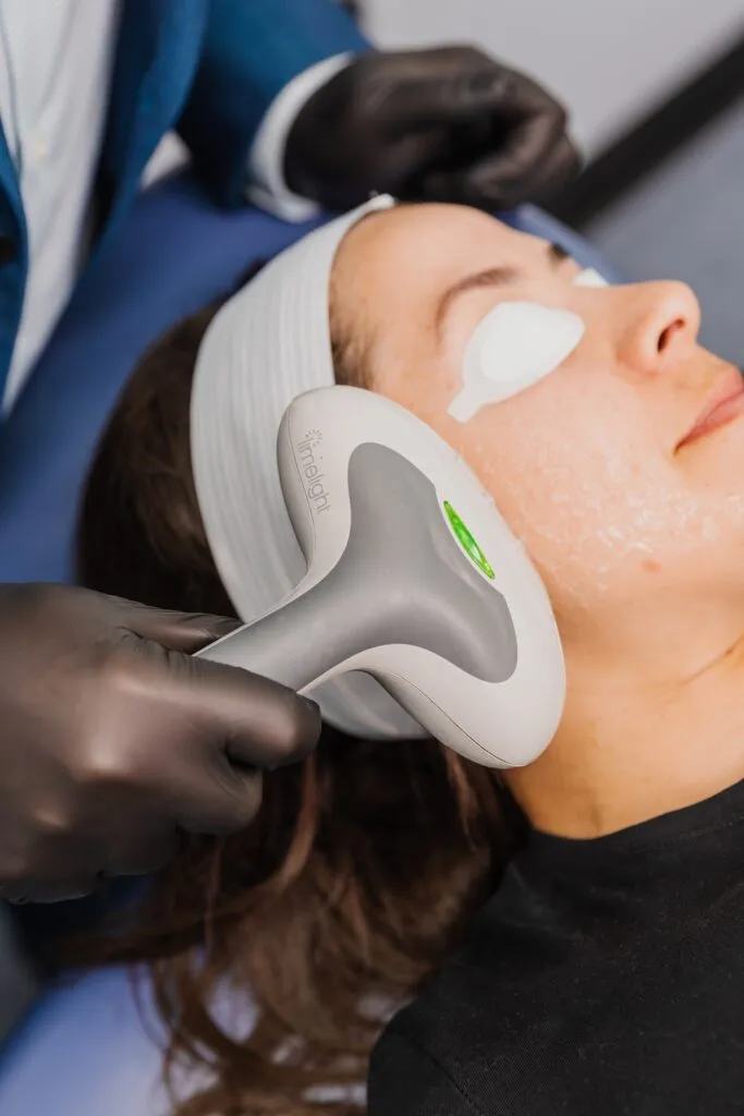 Woman receiving facial treatment with a laser device at a plastic surgery center.