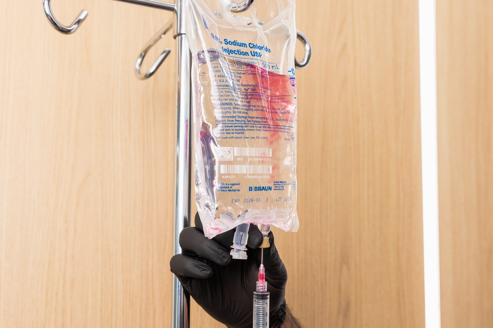 IV drip with black-gloved hand adjusting syringe in medical setting.