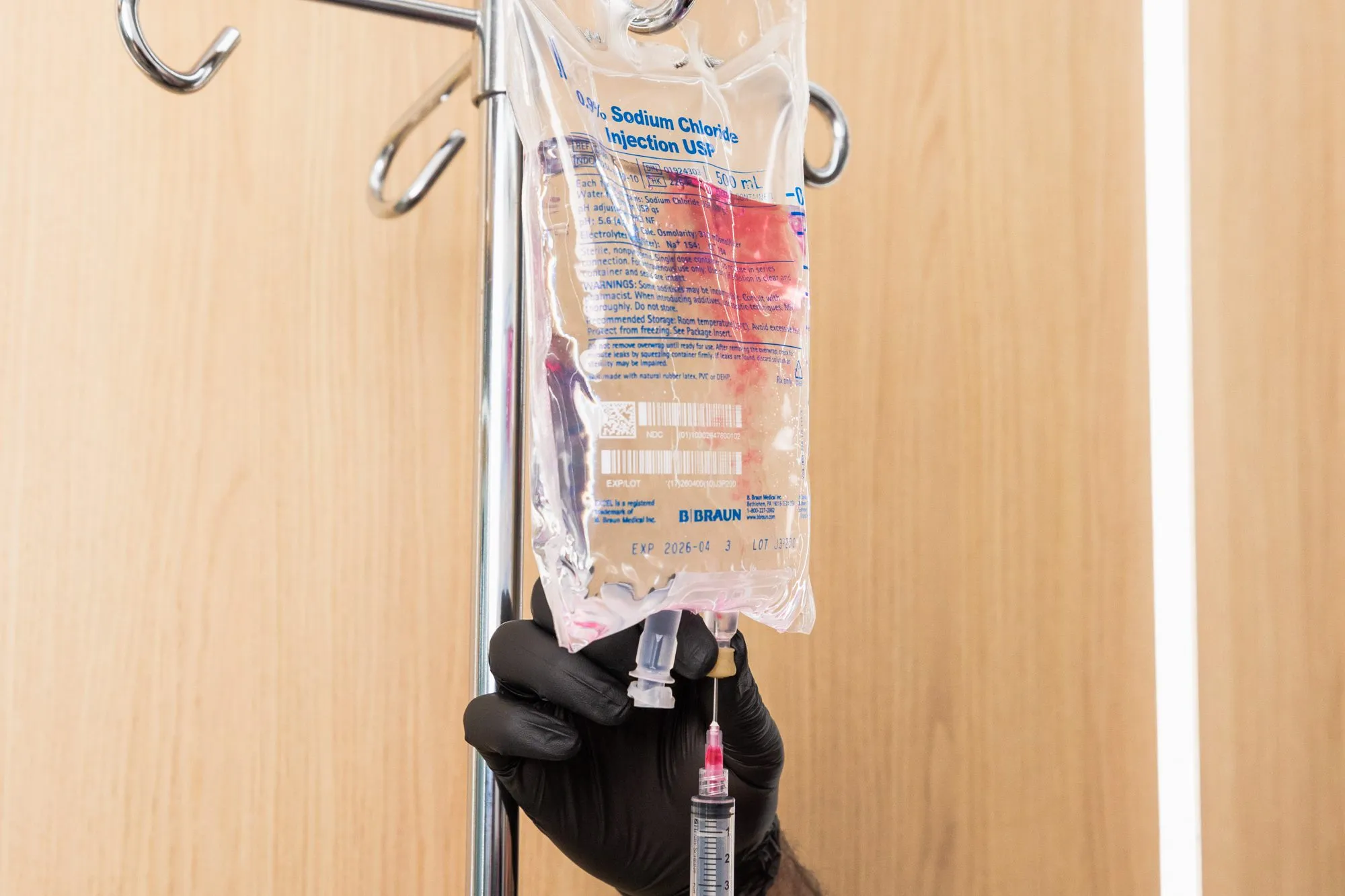 IV drip with black-gloved hand adjusting syringe in medical setting.