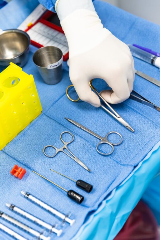Plastic surgery tools on a surgical tray with a gloved hand picking up scissors.