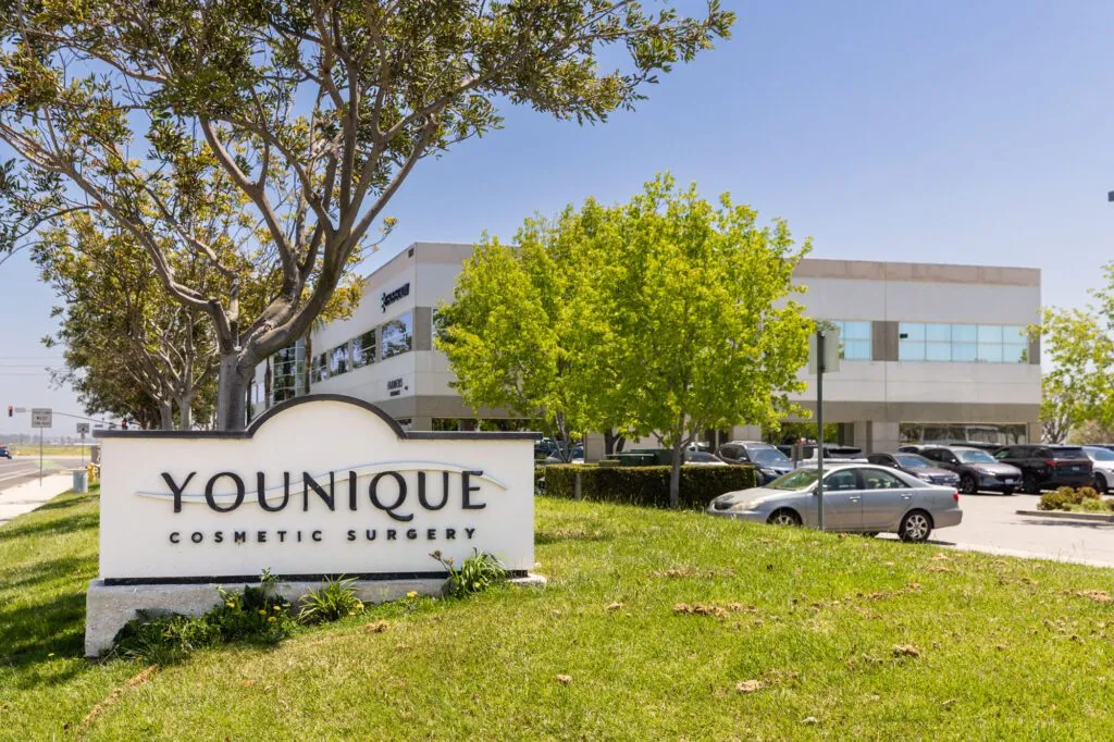 Younique Cosmetic Surgery Center building and sign with trees and parked cars.