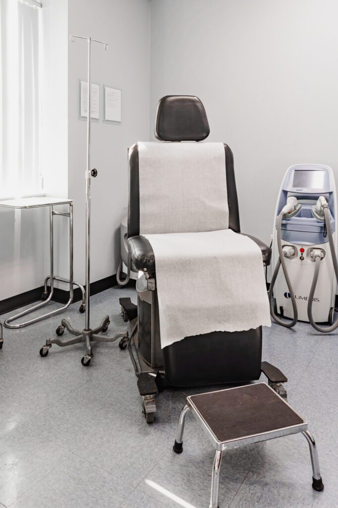 Modern plastic surgery consultation room with chair and medical equipment.