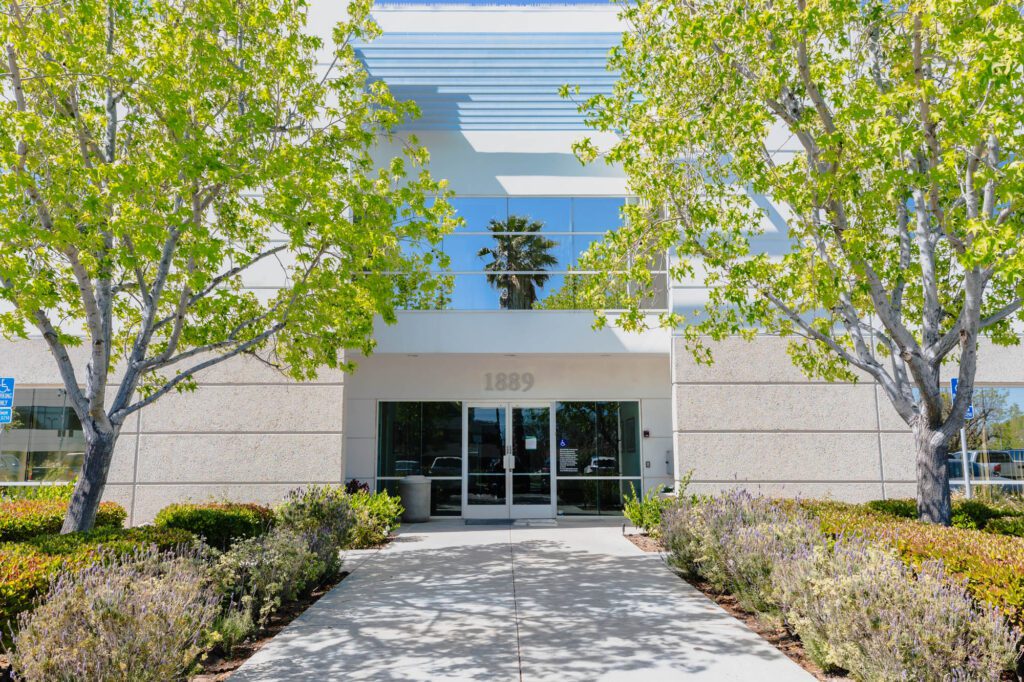 Modern exterior of a plastic surgery center with trees and shrubs.