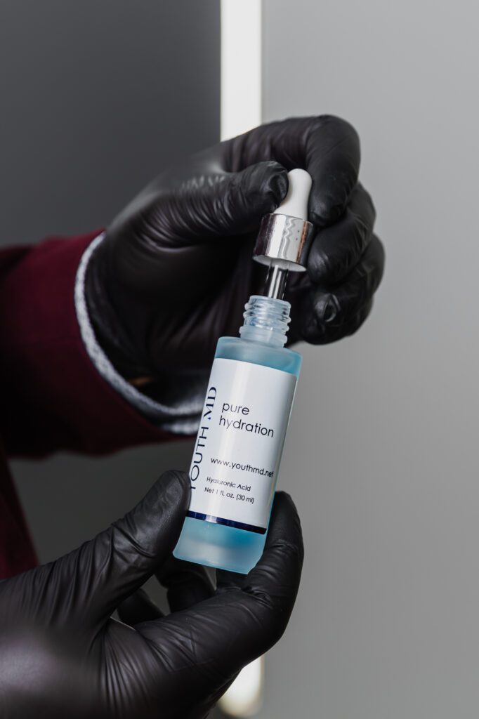 Gloved hands holding a bottle of hyaluronic acid serum with a dropper at a plastic surgery clinic.