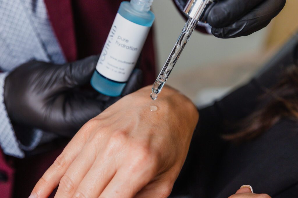 Gloved hand applying hydrating serum on skin with dropper.