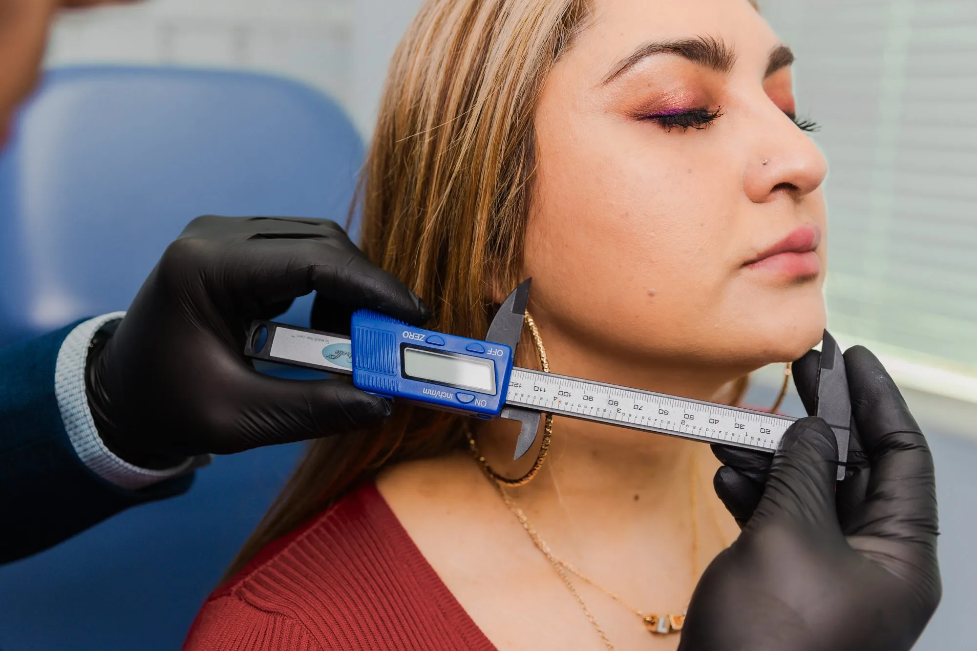 Plastic surgeon measuring woman's chin with calipers in consultation room.