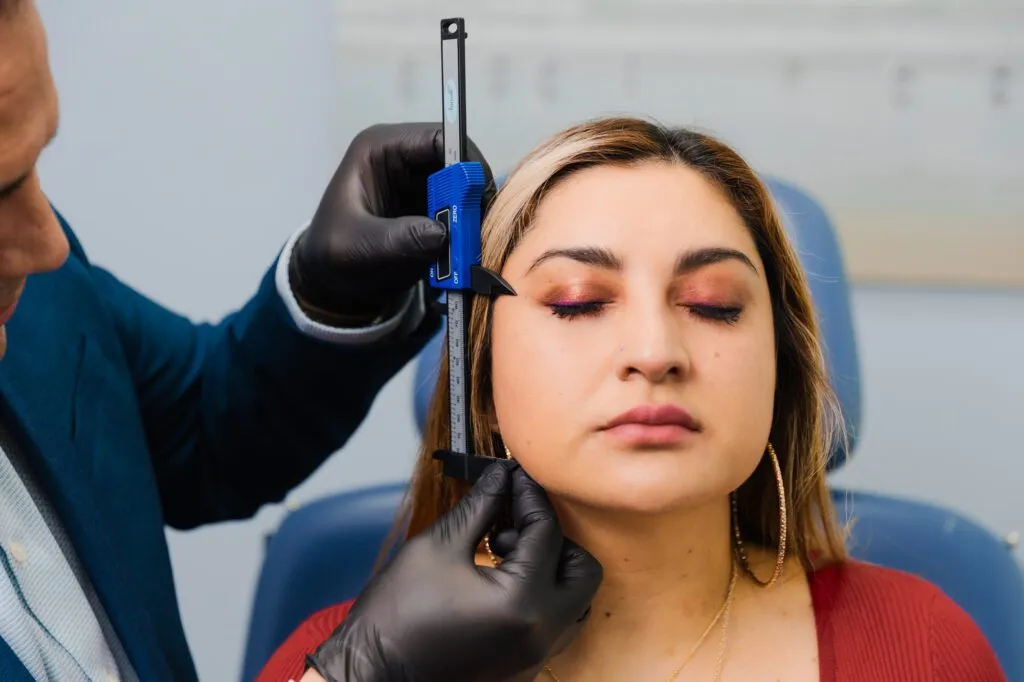 Plastic surgeon measuring woman's facial features with calipers in consultation room.