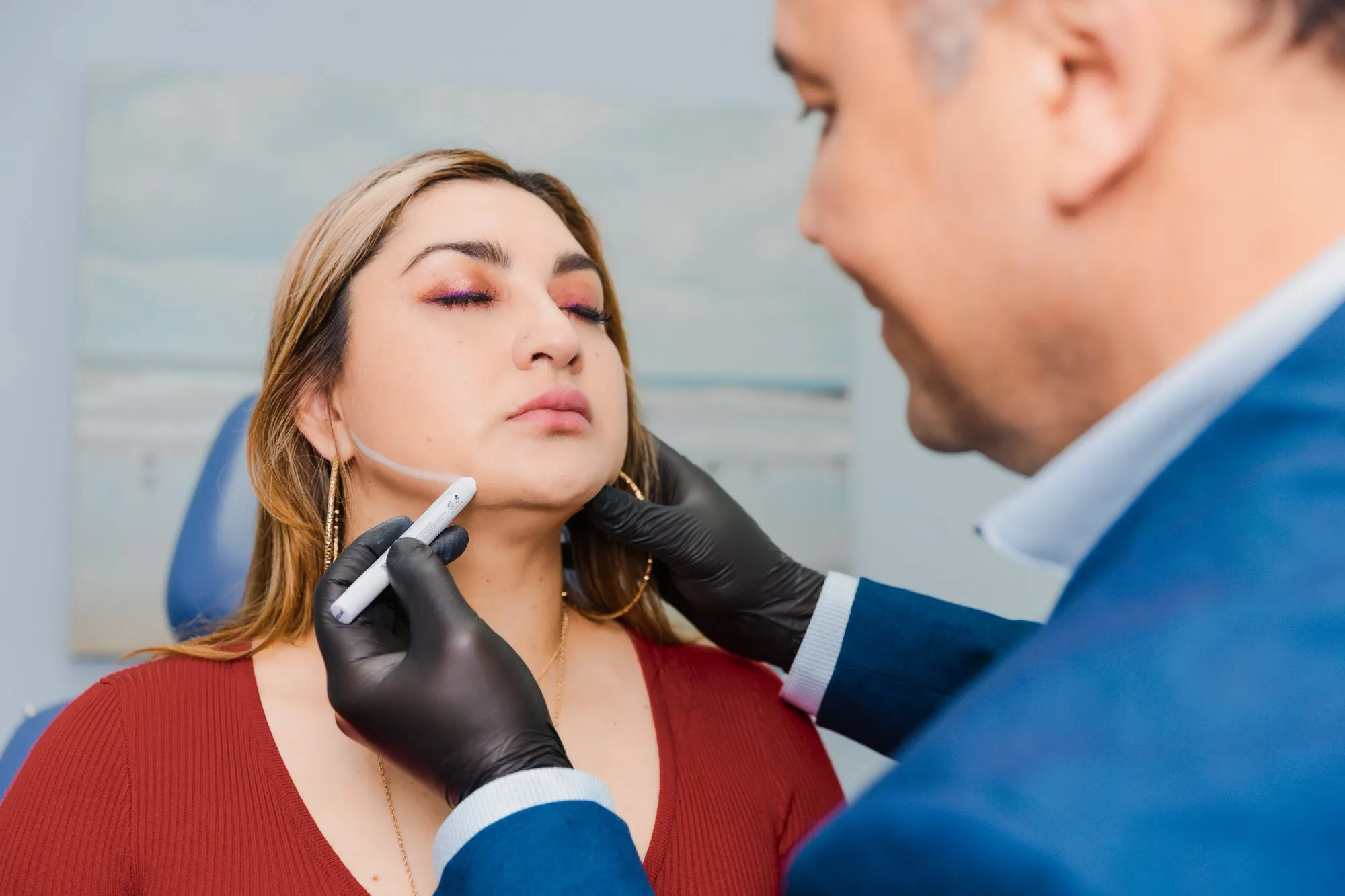 Plastic surgeon outlining patient's jawline with a marker before cosmetic procedure.