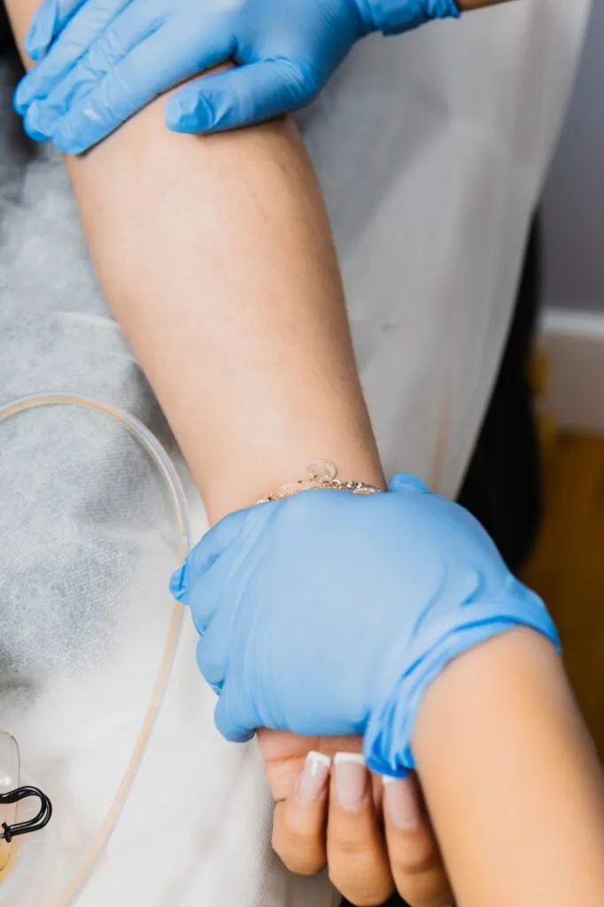 Healthcare professional wearing blue gloves administering an intravenous drip on a patient in a clinical setting.