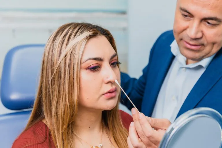 Person receiving a nasal swab examination from a medical professional in an office setting.