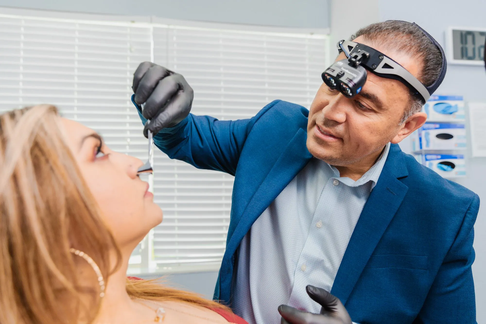Doctor examining a patient's nose using medical equipment in a clinical setting.