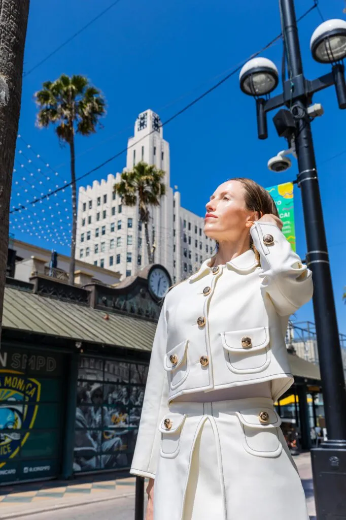 Woman in white outfit with smooth skin standing downtown under a clear blue sky.