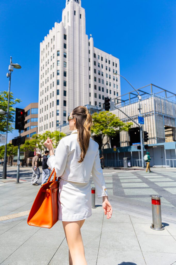 Woman in a stylish white outfit walking confidently in an urban setting.