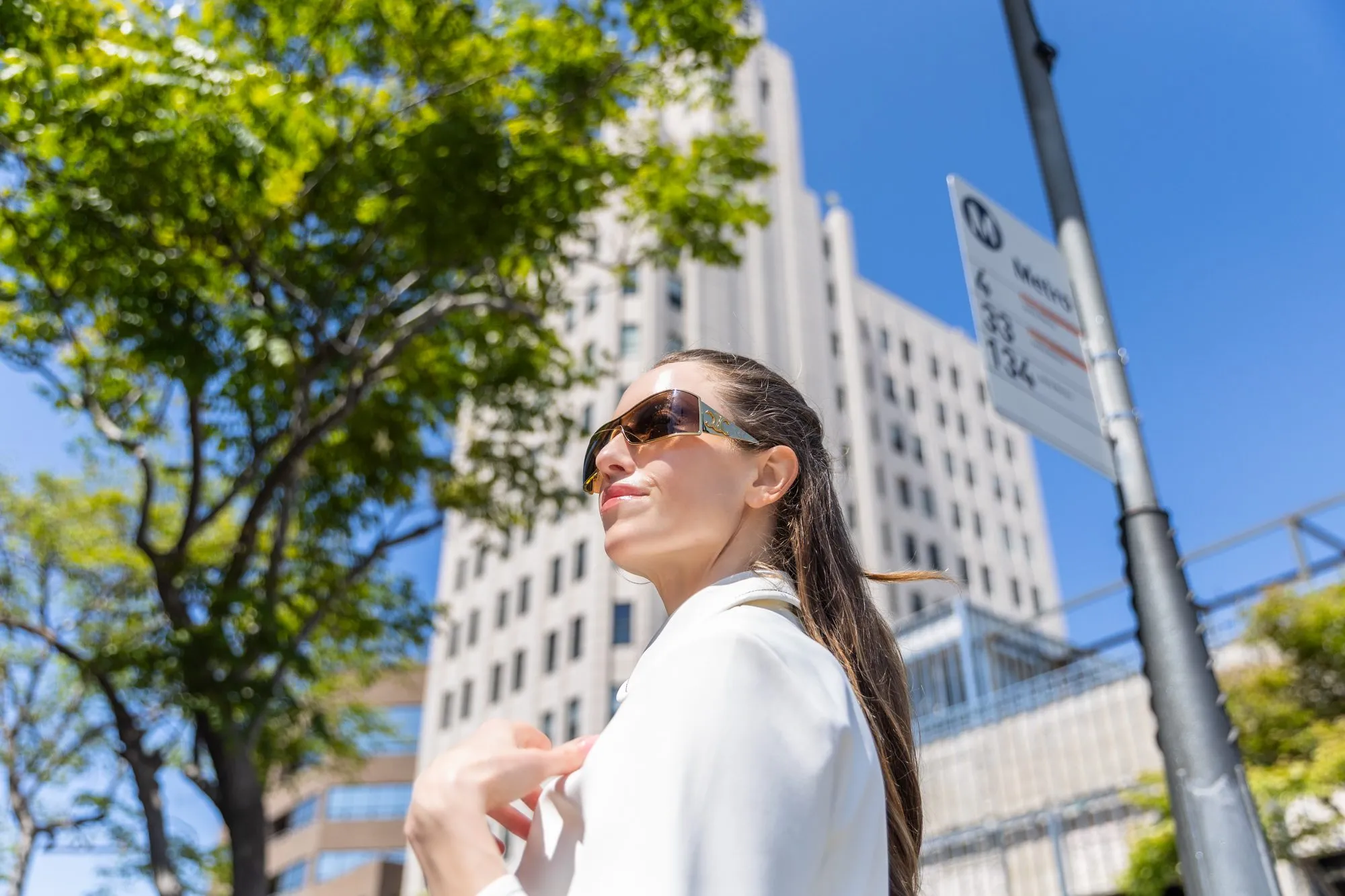 Woman in sunglasses confidently standing outside a modern building under a clear blue sky.