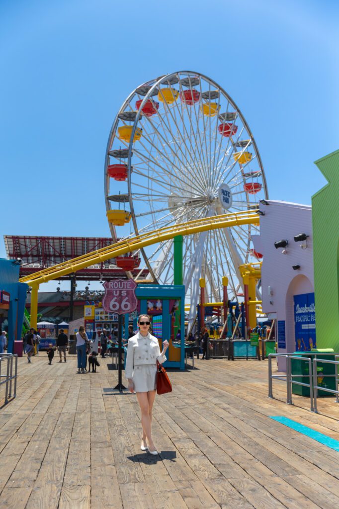 Woman walking on a boardwalk near a Ferris wheel, representing confidence and beauty.