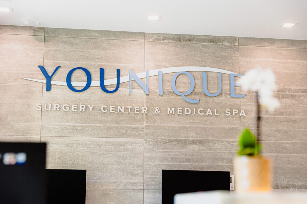 "Younique Surgery Center and Medical Spa logo on a modern interior wall."