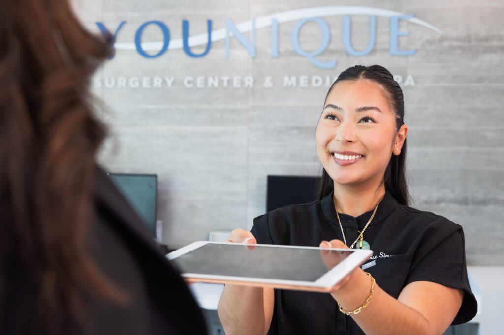 Smiling receptionist at a plastic surgery center holding a tablet.