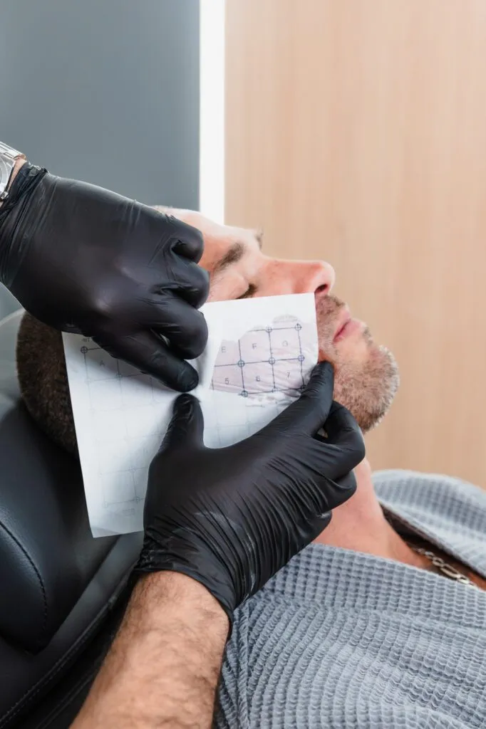 Plastic surgeon preparing male patient with facial grid for cosmetic procedure.