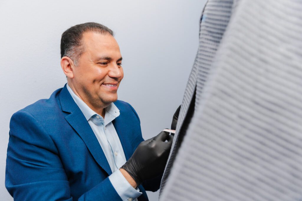Plastic surgeon smiling while performing a procedure in an office setting.