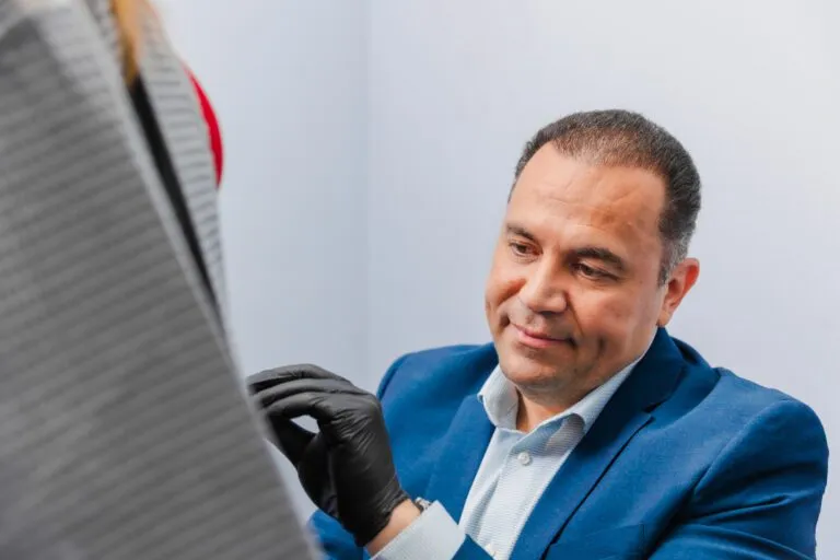 Plastic surgeon in a blue suit examining a patient in a consultation room.