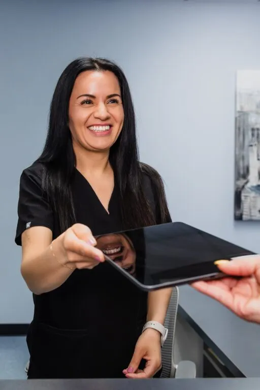 Receptionist at a plastic surgery center handing a tablet to a patient.