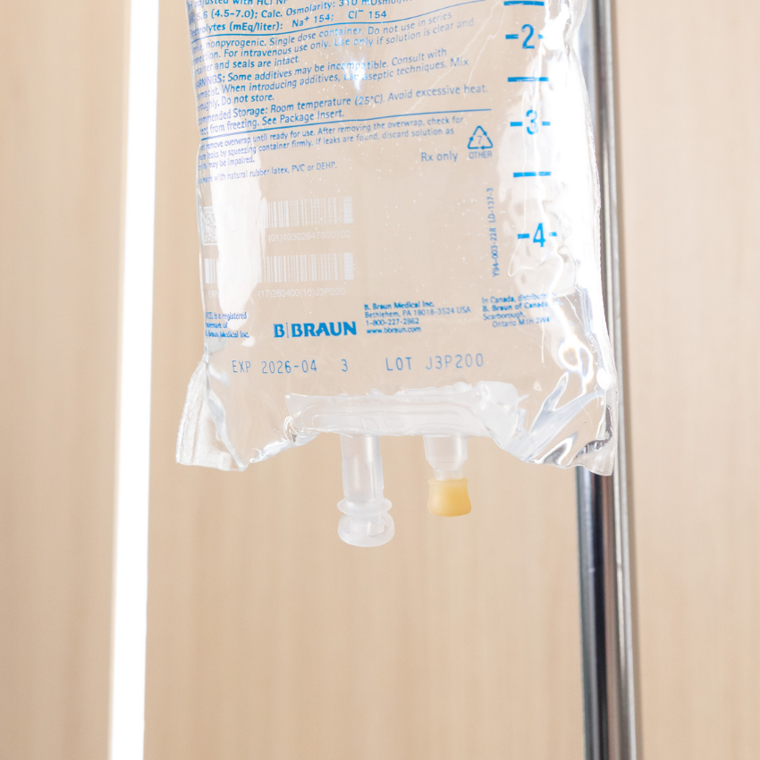 Person receiving IV therapy while using a smartphone in a clinic setting.